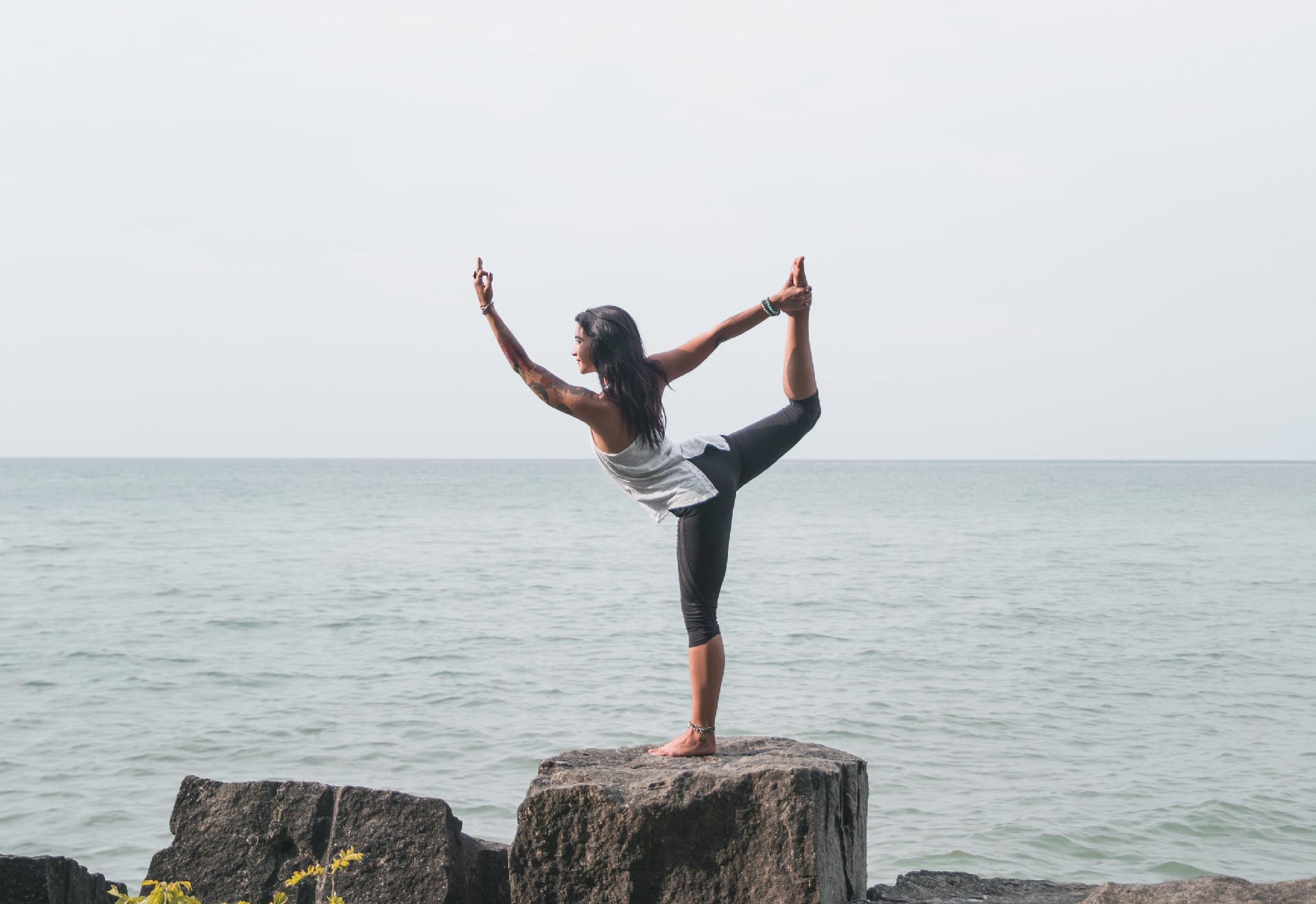 Woman balancing on a rock in a yoga pose near the ocean.