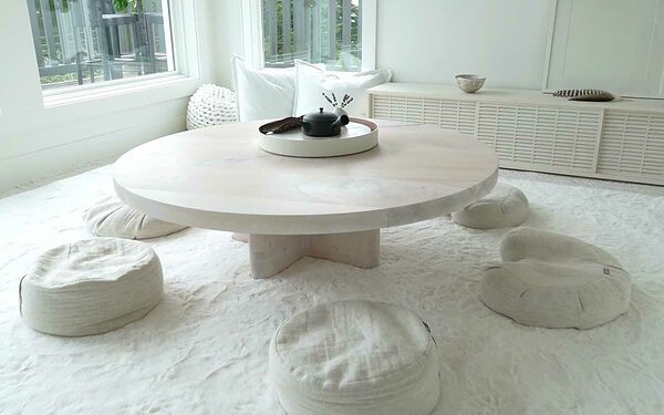 A round wood table surrounding by meditation cushions.