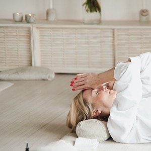 Blonde woman laying in ceremony room with prayer hands to forehead